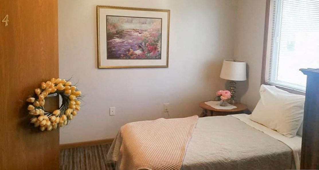 A bedroom with a bed, a wreath, a lamp, and a painting on the wall.